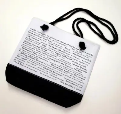 A white bag with black handles and a black strap.